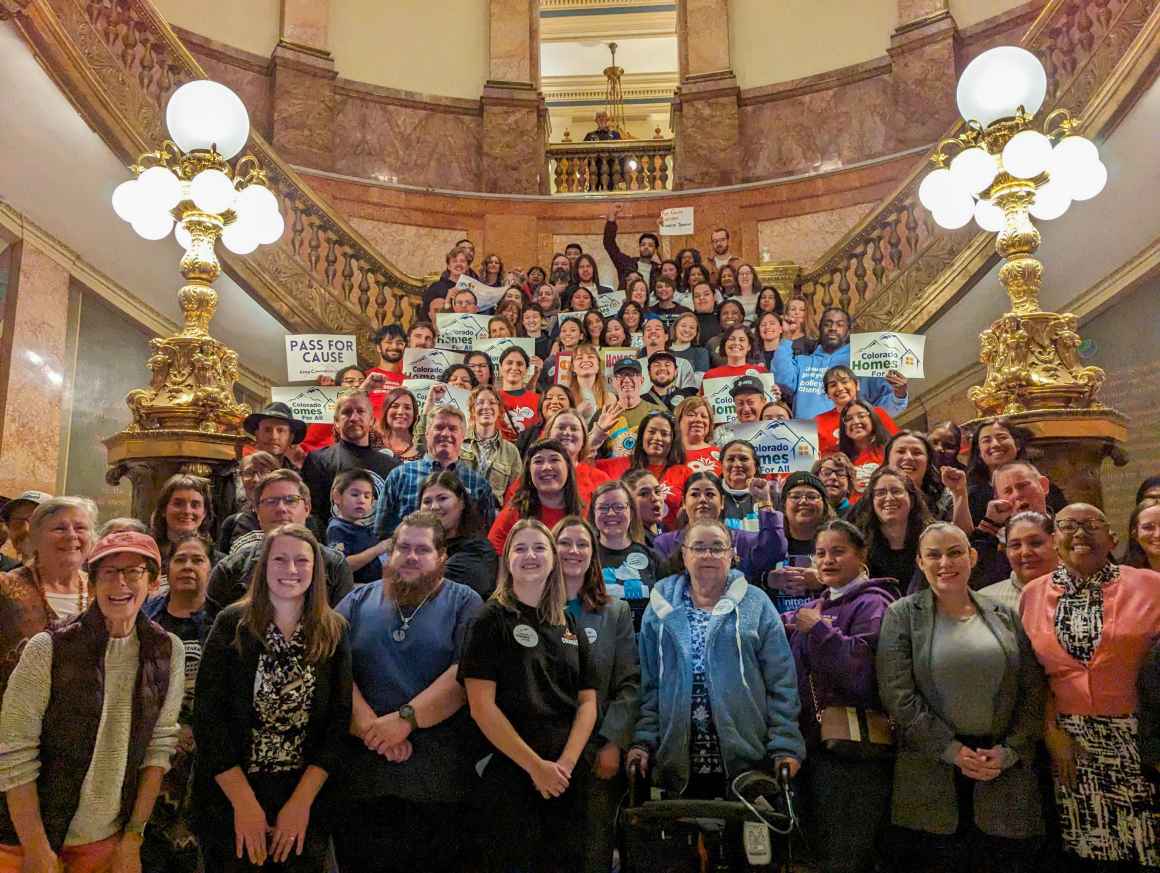 Photo of a crowd of people standing on the stairs of the Colorado state capitol rotunda and holding up signs